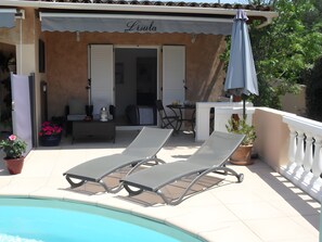 A poolside area with lounge chairs, a table, and a potted plant.