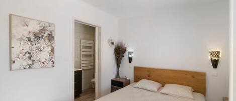 Een slaapkamer met een bed, een nachtkastje, een wandlamp en een deur naar een badkamer.