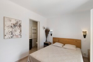 Une chambre à coucher comprenant un lit, une table de chevet, un luminaire fixé au mur et une porte donnant accès à une salle de bain.