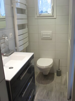 A modern bathroom with a white sink, a toilet, and a window above the toilet.