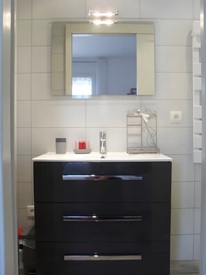 A bathroom with a white vanity, a mirror, and a light fixture above the mirror. - Bed and Breakfast "L'isula" with Mountain View, Wi-Fi, and Air Conditioning (Porto-Vecchio)