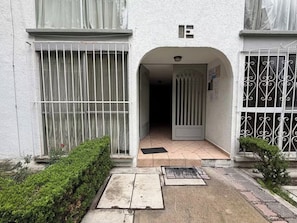 A building entrance with a gated driveway, a small garden area, and a tiled pathway leading to the entrance. - Apartment near Benito Juárez Airport (Ciudad de México)