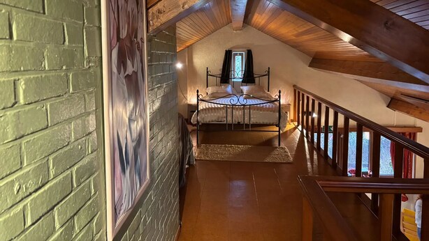 Ein Schlafzimmer mit schrägverdachter Decke, einem Bett, einem Fenster und einer Treppe, die in eine weitere Ebene führt.