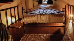 Ein Einzelbett mit Metallgestell in einem Zimmer mit schrägen Decken und einem fensterbelaubten Fenster.