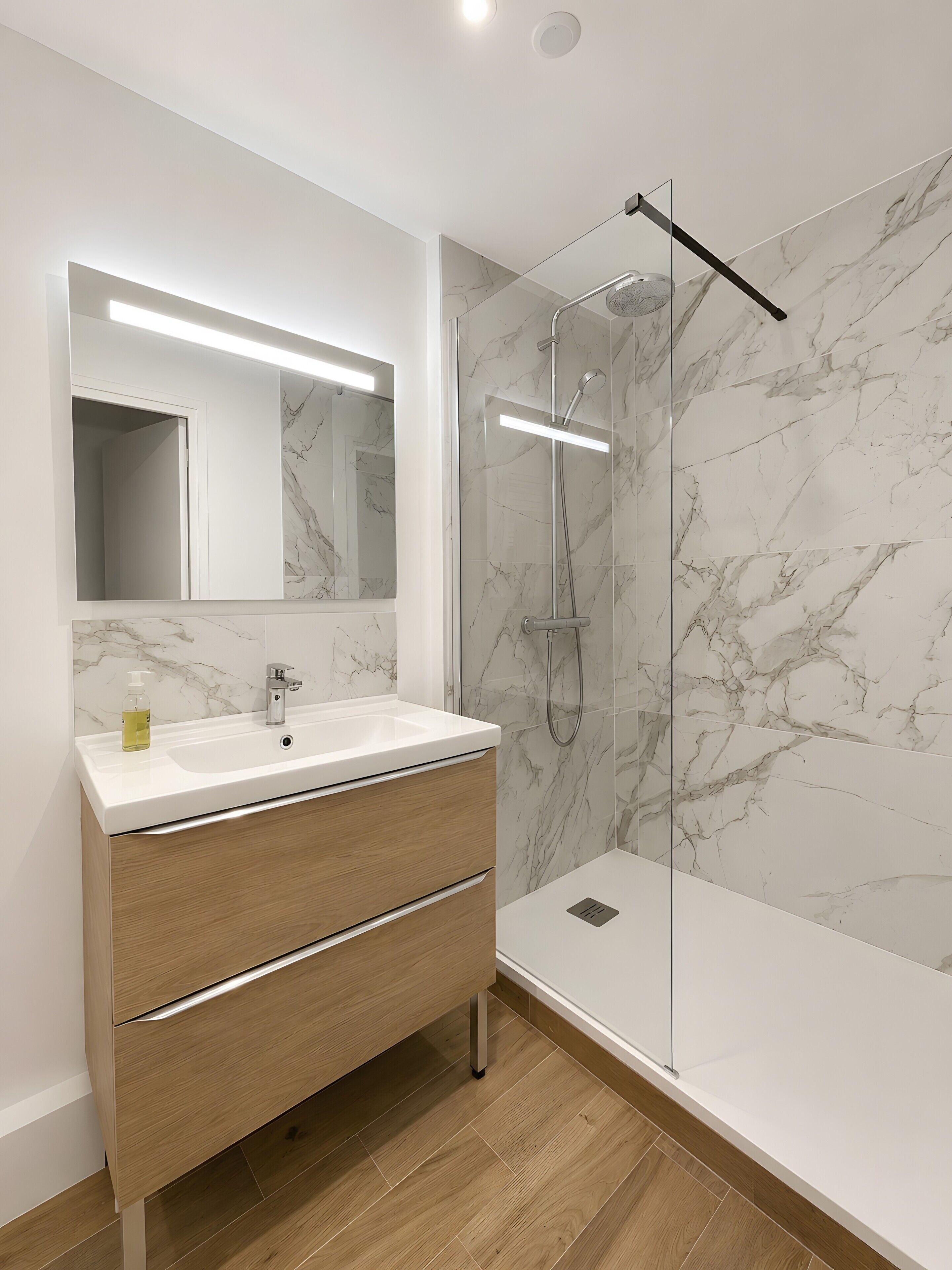 Une salle de bain moderne avec un mur en marbre, un lavabo blanc et une douche à parois de verre.