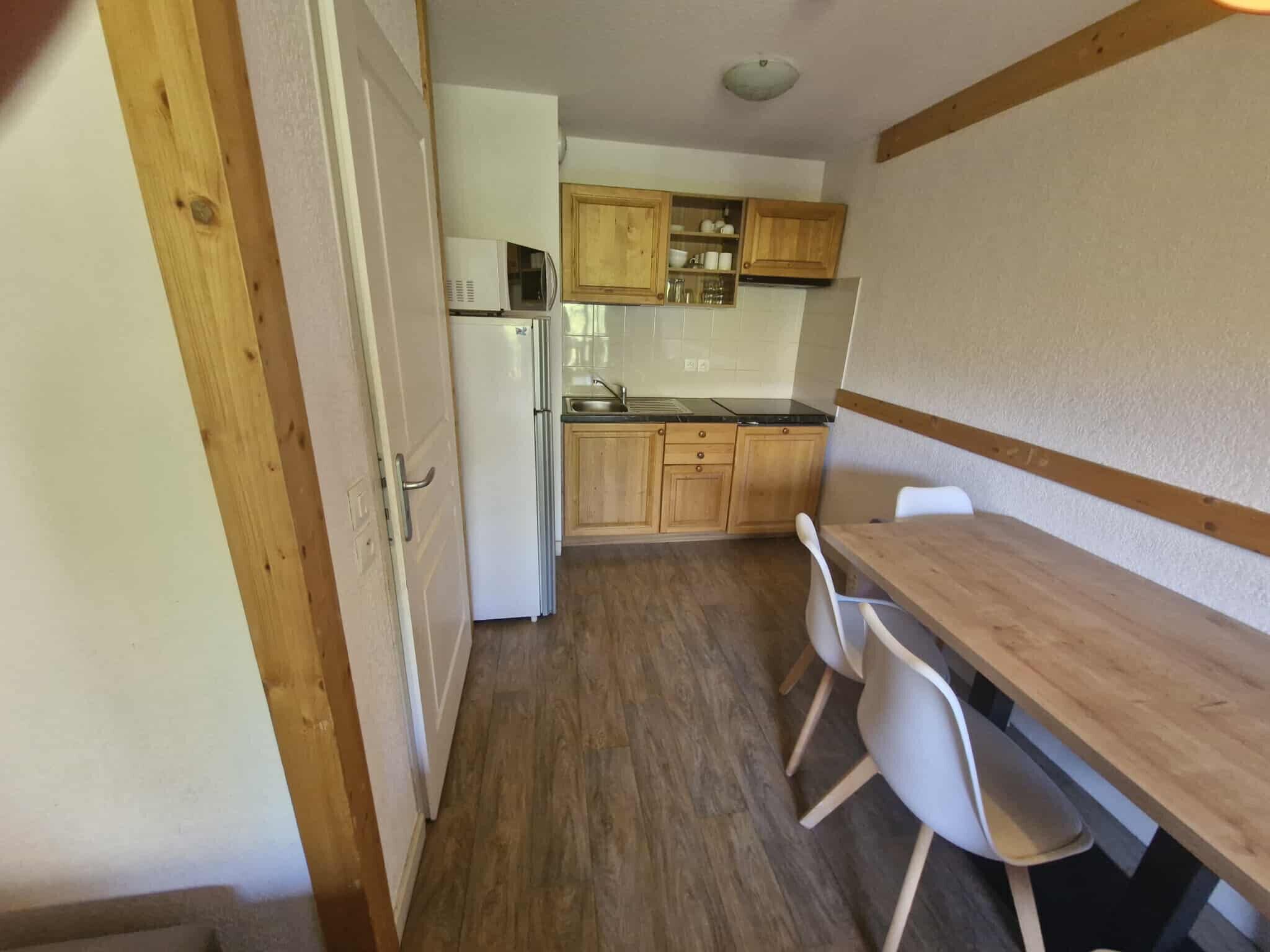 A compact kitchen with wooden cabinets, a refrigerator, and a dining area with a table and chairs.