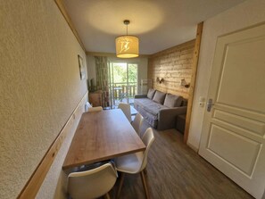 A cozy room with a wooden dining table, chairs, a sofa, and a large window. - Apartment with balcony and heated indoor swimming pool (Saint-Sorlin-d´Arves)