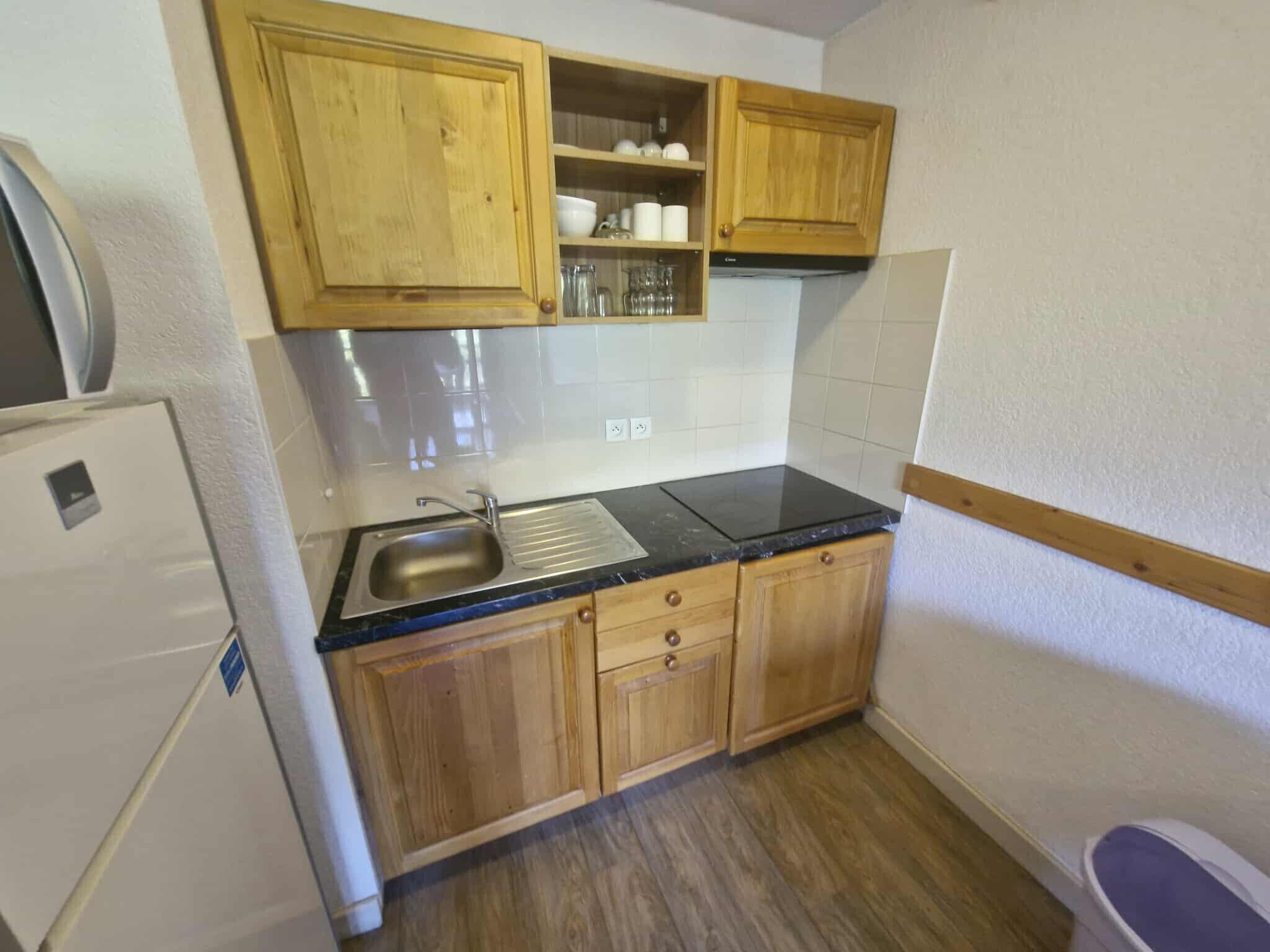 A compact kitchen with wooden cabinets, a black countertop, and a stainless steel sink.