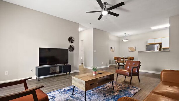 Un salon moderne doté d’un téléviseur à écran plat, d’un ventilateur de plafond et d’un coin repas avec des chaises et une table.