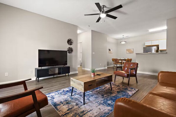Ein modernes Wohnzimmer mit Flachbildfernseher, Deckenventilator und Essbereich mit Stühlen und Tisch.