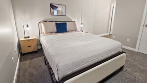 Une chambre à coucher avec un lit, des tables de chevet, un tableau accroché au mur et une porte.