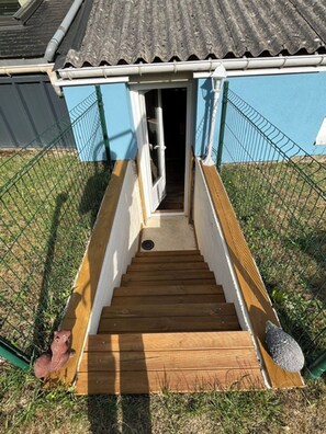A wooden staircase leading to a building entrance with a metal fence surrounding the area. - The Blue House in the Heart of St. Valéry-sur-Somme (St Valéry sur Somme)