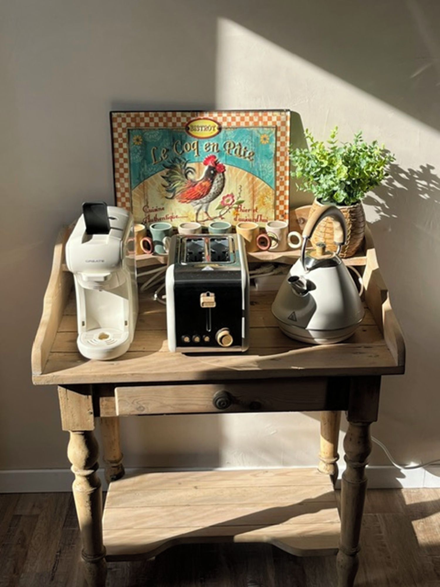 A wooden table with a rustic design, a vintage toaster, a white electric kettle, and a box labeled 'Le Coq en Pointe.'