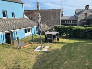 A residential backyard with a fenced area, a table and chairs, and a dog house. - The Blue House in the Heart of St. Valéry-sur-Somme (St Valéry sur Somme)