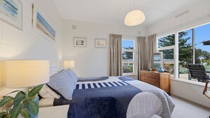 Un dormitorio con cama, lámparas de noche, cómoda, silla y ventana con vista a follaje.