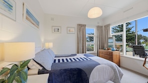 A bedroom with a bed, bedside lamps, a dresser, a chair, and a window with a view of greenery. - 25 Captain Sturt Rd, Hindmarsh Island (Hindmarsh Island)