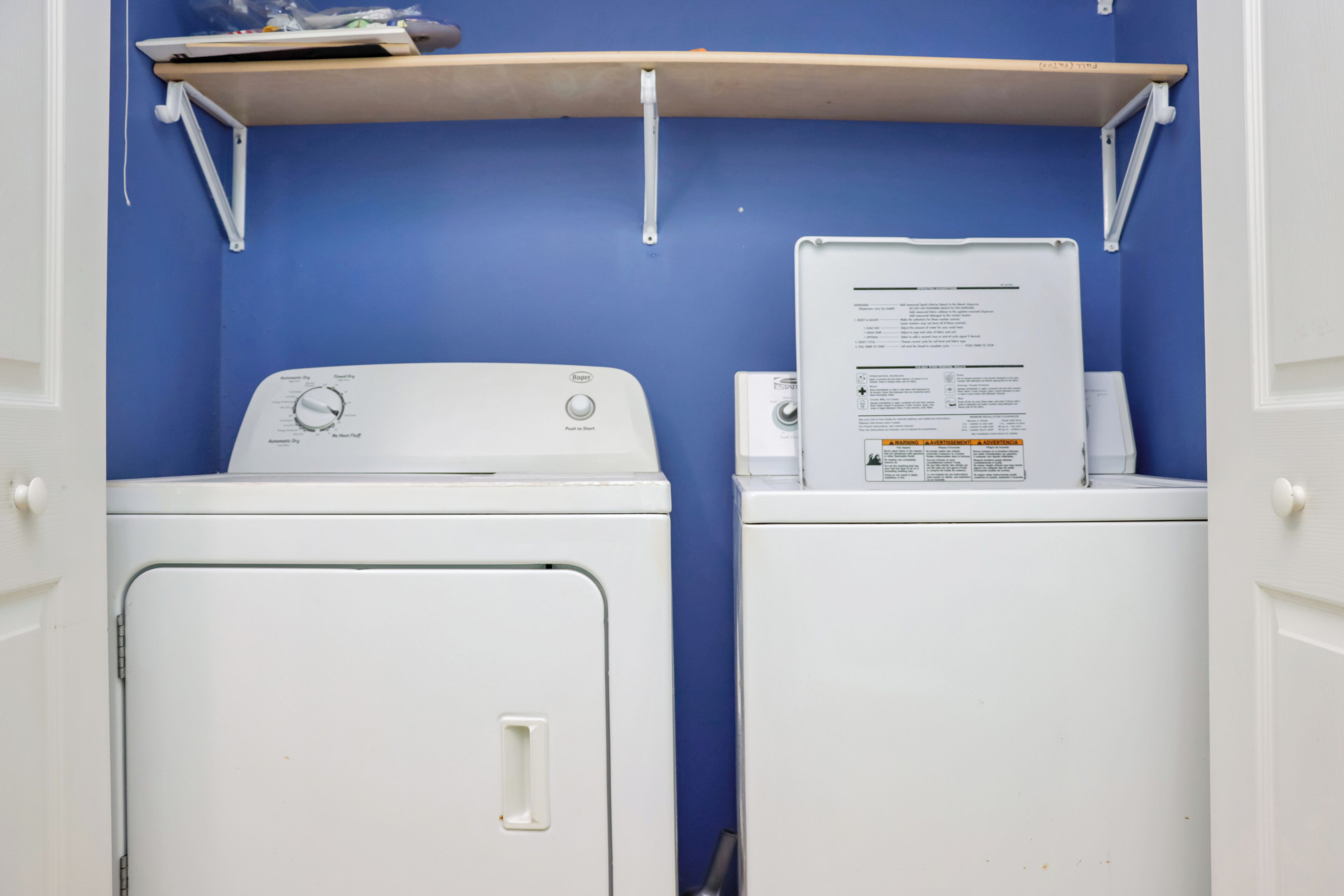 Une buanderie avec deux machines à laver blanches et une étagère au-dessus.