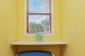 A room with a yellow wall, a window with blinds, a white shelf, and a blue object on the floor. - Sunny Daze | Steps to Beach | Community Pool | Pet Friendly (Indian Pass)