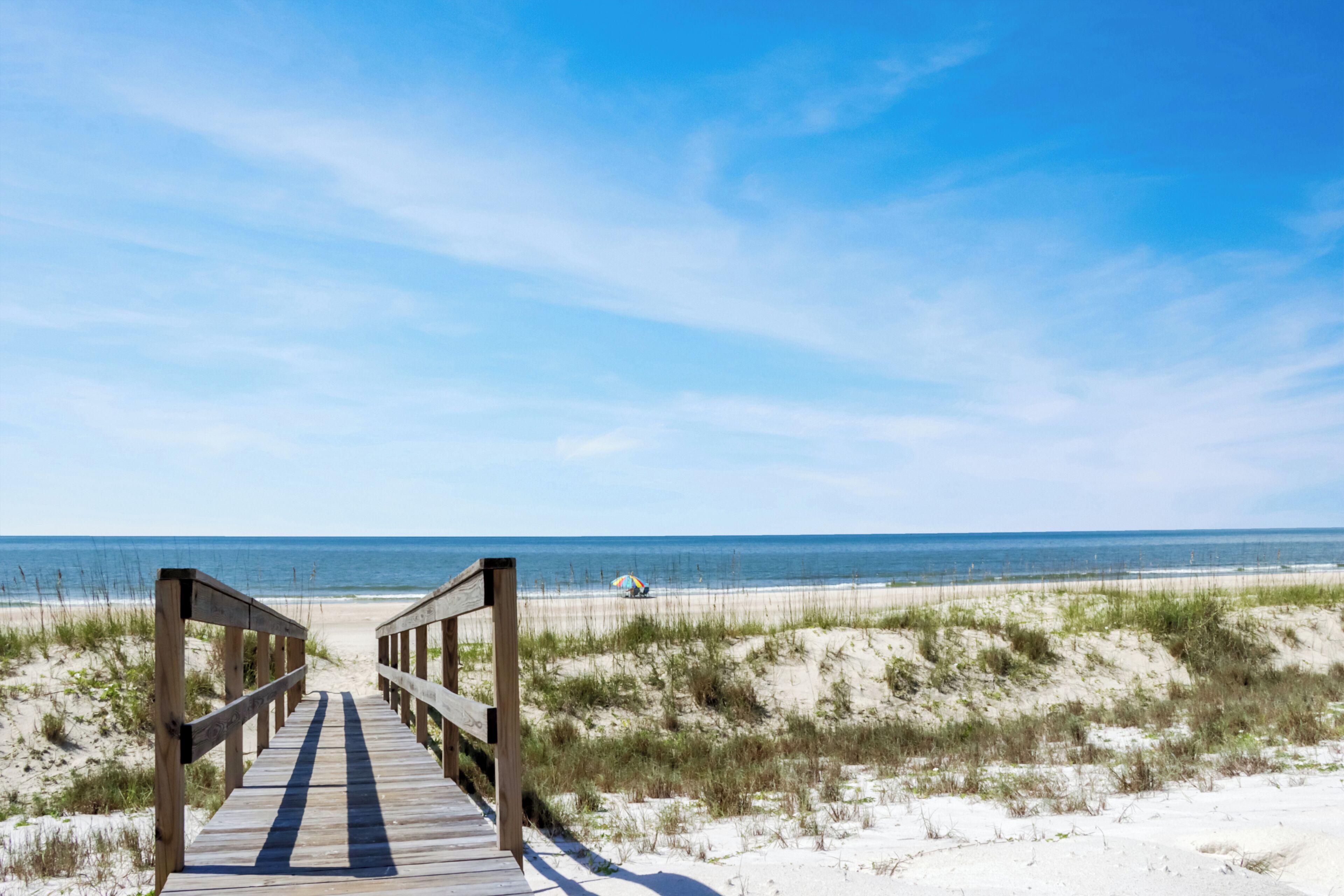 A wooden boardwalk leading to a beach with sand dunes and the ocean in the background.