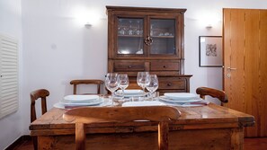 Una mesa de comedor de madera dispuesta con platos, vasos y cubiertos, acompañada de sillas, y un armario de madera al fondo.