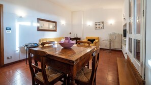A dining area with a wooden table and chairs, a bowl, and a vase. There is a sofa and a small table with a lamp in the background. - San Petronio Vecchio 57 (Bologna)