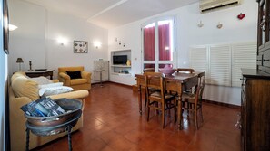 Un saló amb un sofà, una taula de dinar amb caires, una televisió i una finestra amb cortines.