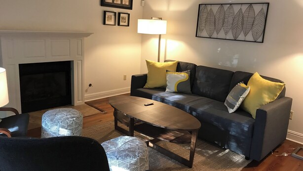 A living room with a fireplace, a sofa with cushions, a coffee table, and a patterned rug. - Hidden Gem! 106 Windstone (Oxford)