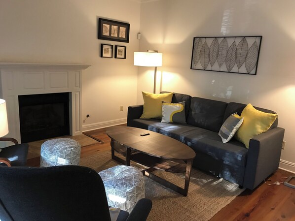 A living room with a fireplace, a sofa with cushions, a coffee table, and a patterned rug. - Hidden Gem! 106 Windstone (Oxford)