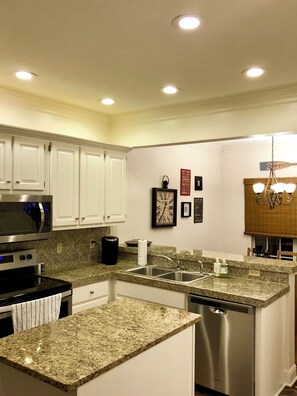 A modern kitchen with white cabinets, granite countertops, stainless steel appliances, and recessed ceiling lights. - Hidden Gem! 106 Windstone (Oxford)