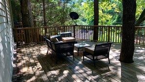 A wooden deck with outdoor furniture, including two chairs and a table, surrounded by trees. - Hidden Gem! 106 Windstone (Oxford)