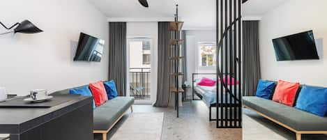 Une chambre d’hôtel moderne équipée d’un canapé, d’une table à manger, d’un téléviseur et d’un ventilateur de plafond.