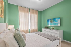 A bedroom with a bed, a nightstand, a dresser, a window with curtains, and a wall-mounted TV. - 5BR home with 5 baths at Windsor Hills (Kissimmee)
