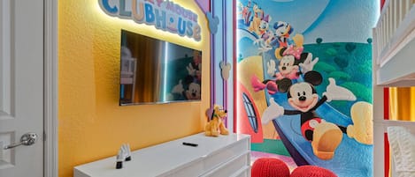 A Mickey Mouse-themed room with a white dresser, a mirror, and a mural of Mickey and Minnie Mouse.