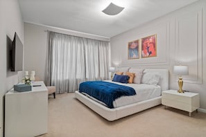 A bedroom with a bed, bedside tables, a desk, a chair, a TV, and curtains. - 5BR home with 5 baths at Windsor Hills (Kissimmee)