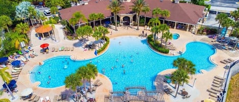 Una amplia piscina al aire libre con varias pistas, rodeada de sillones y sombrillas.