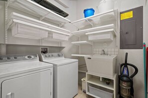 A laundry room with stacked washer and dryer units, shelves with baskets, and a vacuum cleaner. - 5BR home with 5 baths at Windsor Hills (Kissimmee)