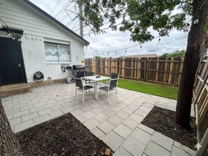 A patio with a table and chairs, a barbecue grill, and a white brick house. - Modern 1BR Near AT&T Stadium + Six Flags (Arlington)