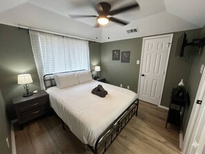 A bedroom with a bed, nightstands, a ceiling fan, a door, and a window with blinds. - Modern 1BR Near AT&T Stadium + Six Flags (Arlington)
