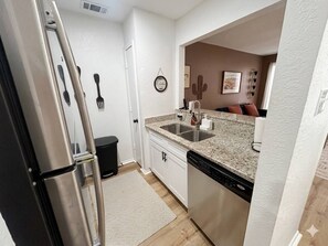 A compact kitchen with a stainless steel refrigerator, a dishwasher, and a granite countertop. - Modern 1BR Near AT&T Stadium + Six Flags (Arlington)