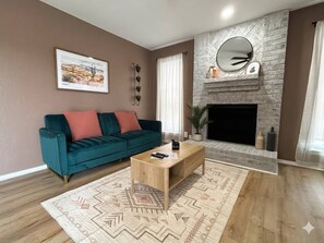 Una sala de estar con sofá, mesa de centro, chimenea y un cuadro en la pared.