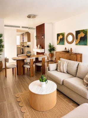 A modern living room with a round coffee table, a sofa, and a dining area with a wooden table and chairs. - Isla Azul Pool & Golf Views, 5 Min to Beach, Near Hard Rock (Punta Cana)