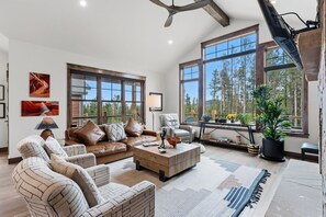 A spacious living room with a large window, a leather sofa, a coffee table, and a fireplace. - Scenic Breck Retreat | Hot Tub & Deck & Firepit (Breckenridge)