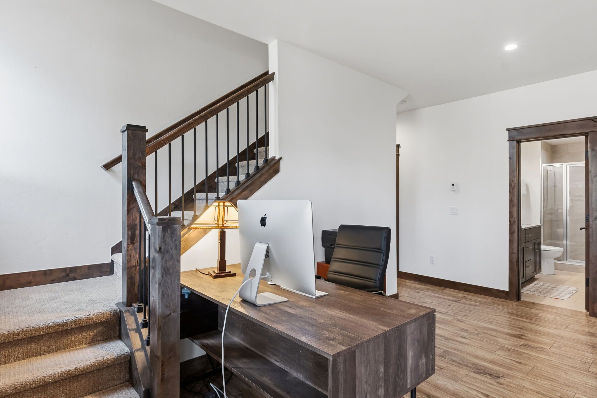 Ein modernes Interieur mit einem Holztisch, zwei Apple iMac Computern, einer Lampe und einem Ledersessel.