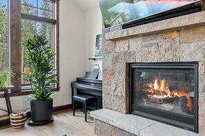 Una sala de estar moderna con chimenea de piedra, un piano y ventanas amplias.
