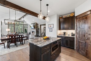 A modern kitchen with dark wood cabinets, a granite countertop, and a central island with a built-in oven. - Scenic Breck Retreat | Hot Tub & Deck & Firepit (Breckenridge)