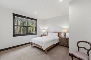Un dormitorio con una ventana grande, una cama, una mesita de noche, una silla y una lámpara.