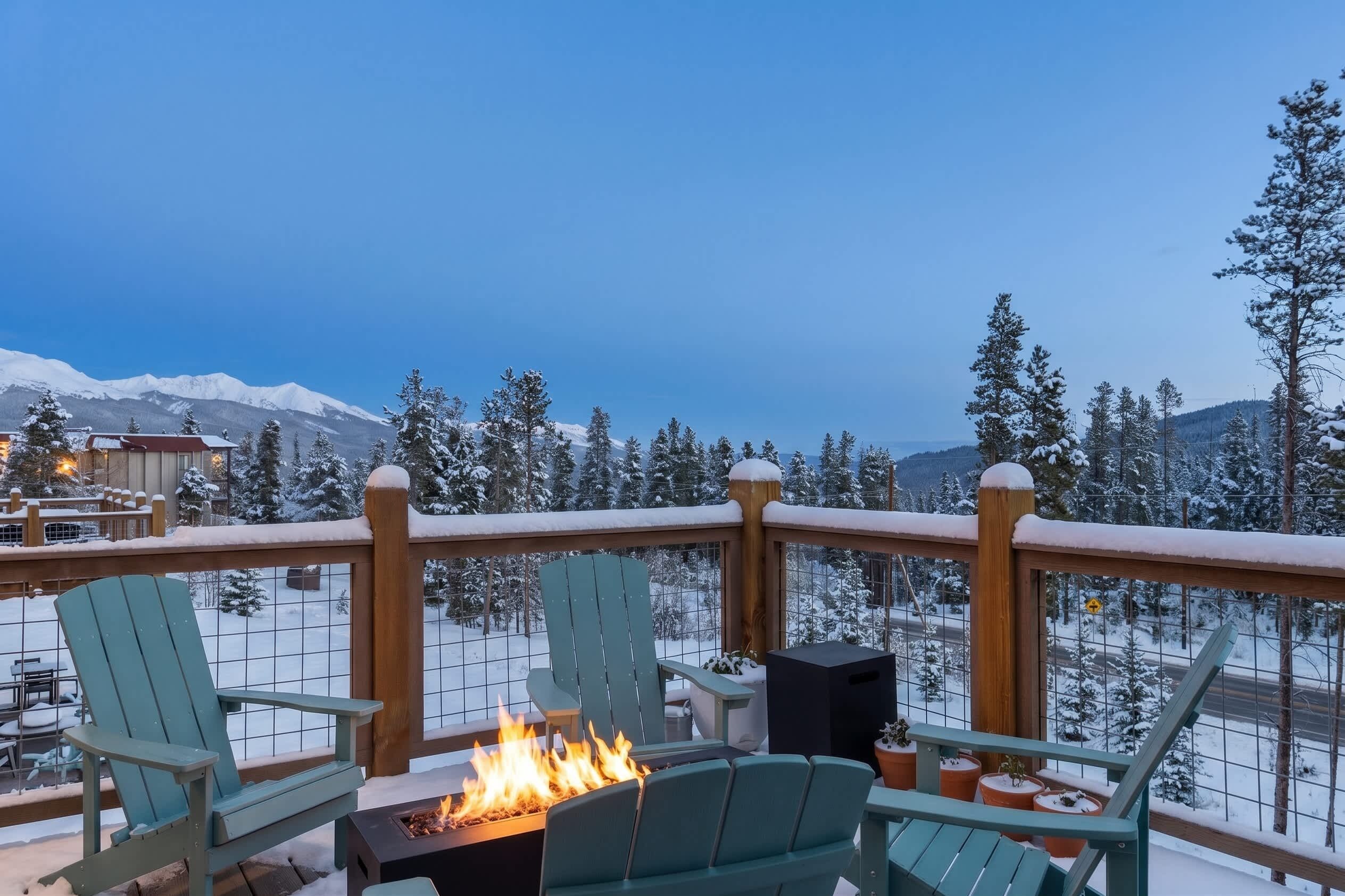 A deck with chairs and a fire pit, overlooking a snowy mountain landscape.
