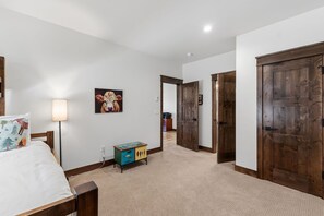 A bedroom with a bed, bedside lamp, dresser, and a door leading to another room. - Scenic Breck Retreat | Hot Tub & Deck & Firepit (Breckenridge)