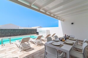 Ein Poolbereich im Freien mit Liegestühlen und einem Esstisch für zwei Personen mit Blick auf einen klaren, blauen Himmel.