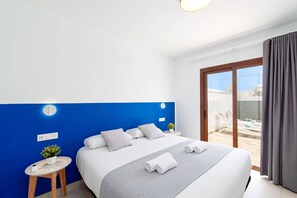 A hotel room with a bed, a small table with a plant, a window with curtains, and a view of the outside. - Villa Naira by Villa Plus (Playa Blanca)